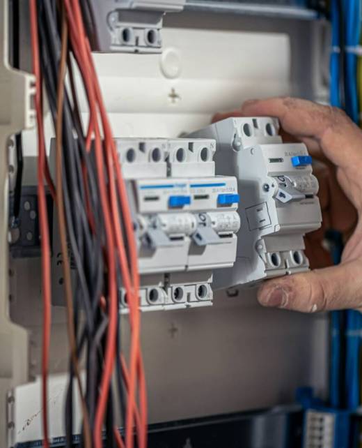 A male electrician works in a switchboard with an electrical connecting cable.